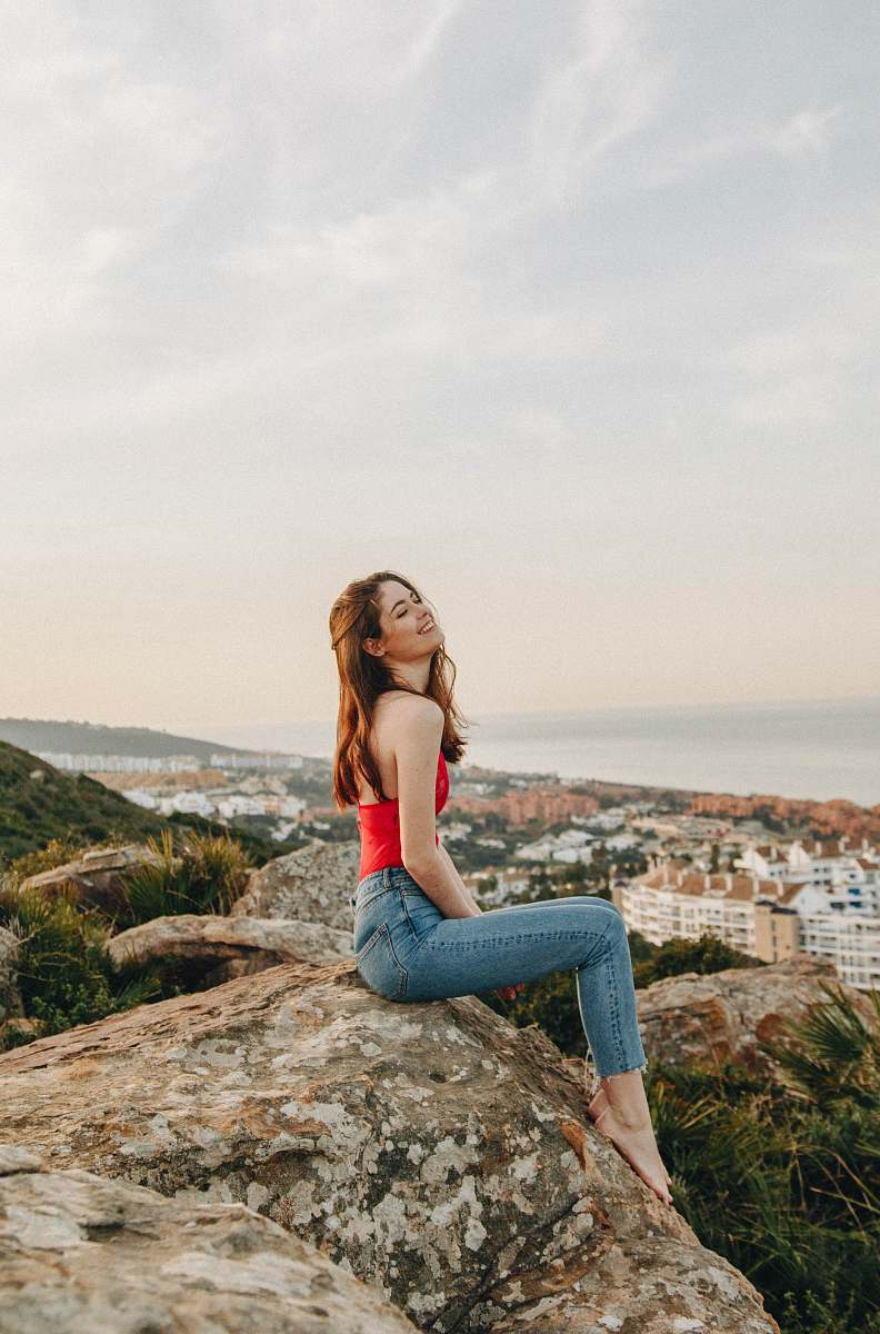 This captivating image features a human woman seated on a rugged rock during a clear daytime, gazing thoughtfully over a picturesque city skyline. The scene exudes serenity and introspection, making it perfect for use in articles and projects that focus on empowerment, urban living, and mindfulness. Ideal for lifestyle blogs, social media posts, and marketing materials aimed at young women seeking inspiration and connection with their surroundings.