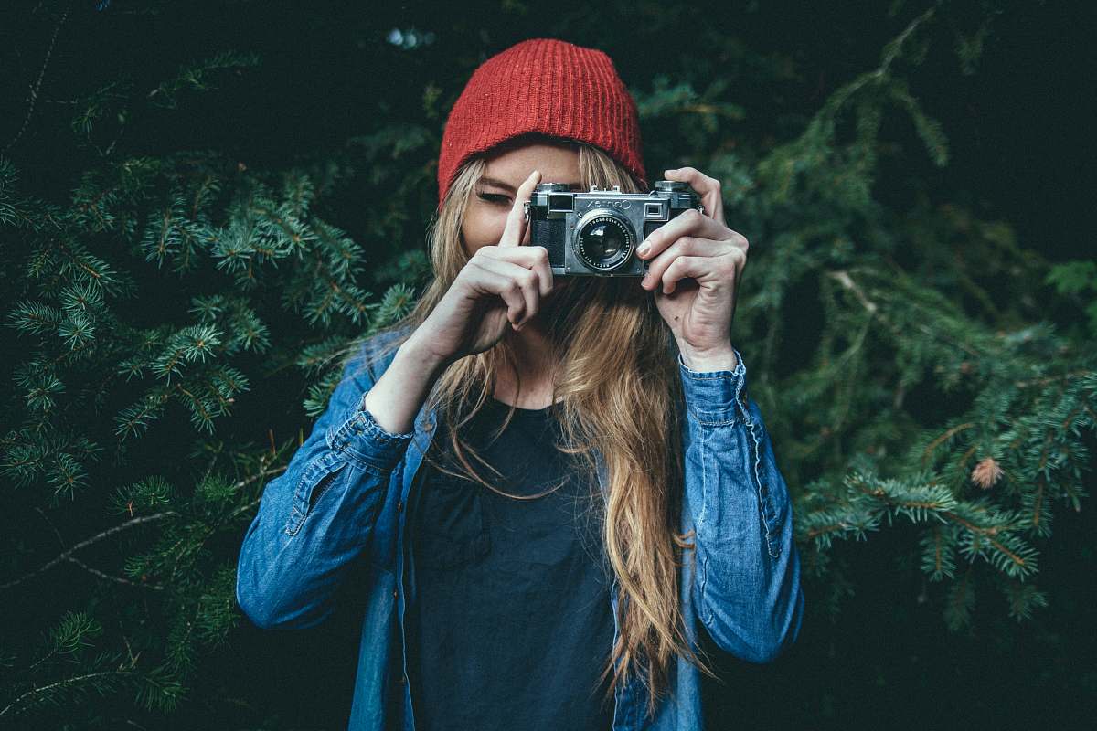 camera woman standing behind green leaf tree holding DSLR camera girl
