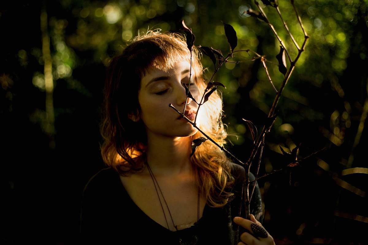 person woman wearing black necklace smelling plant during daytime woman