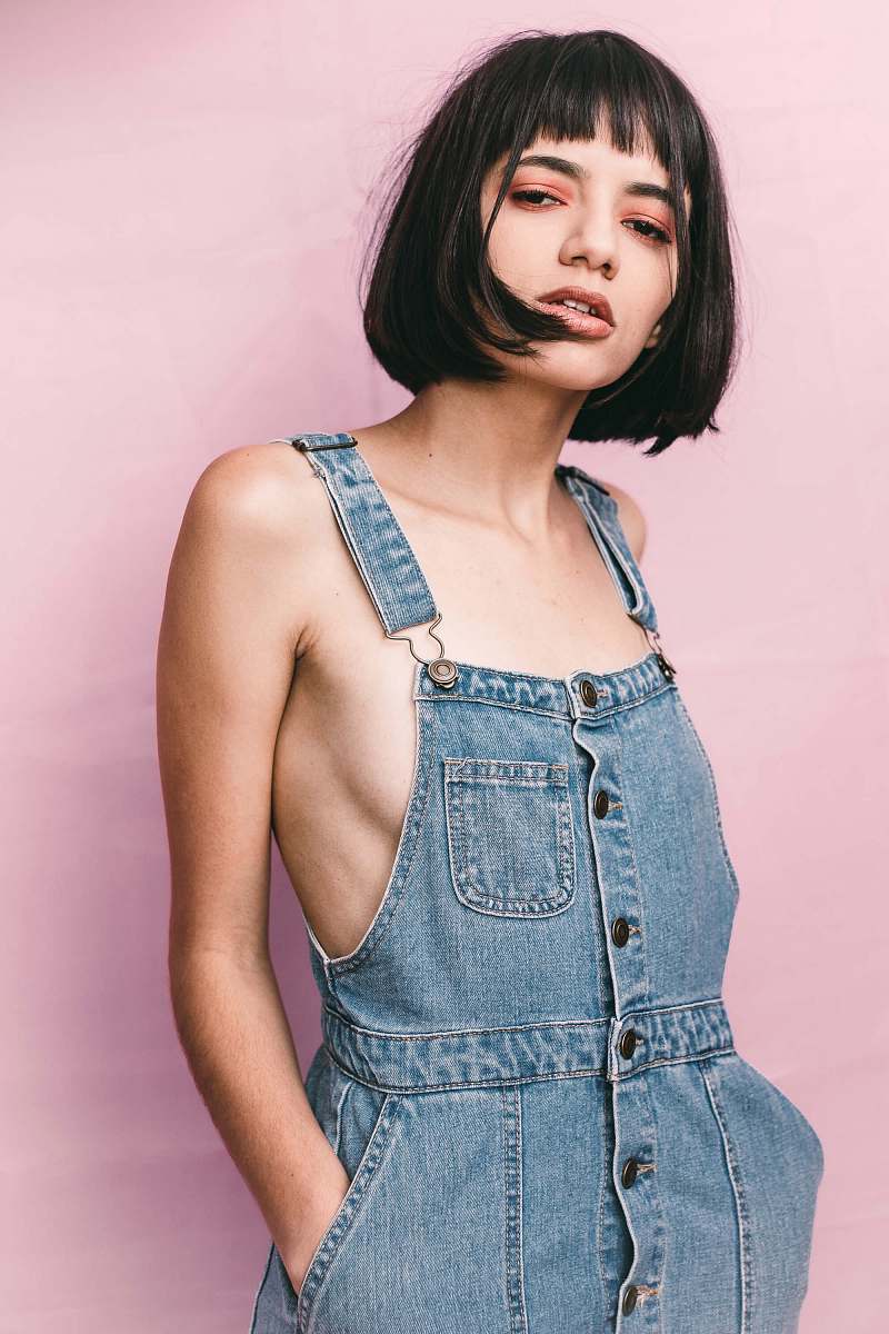 person woman wearing blue bib-and-brace denim bottoms with two hands inside pocket denim