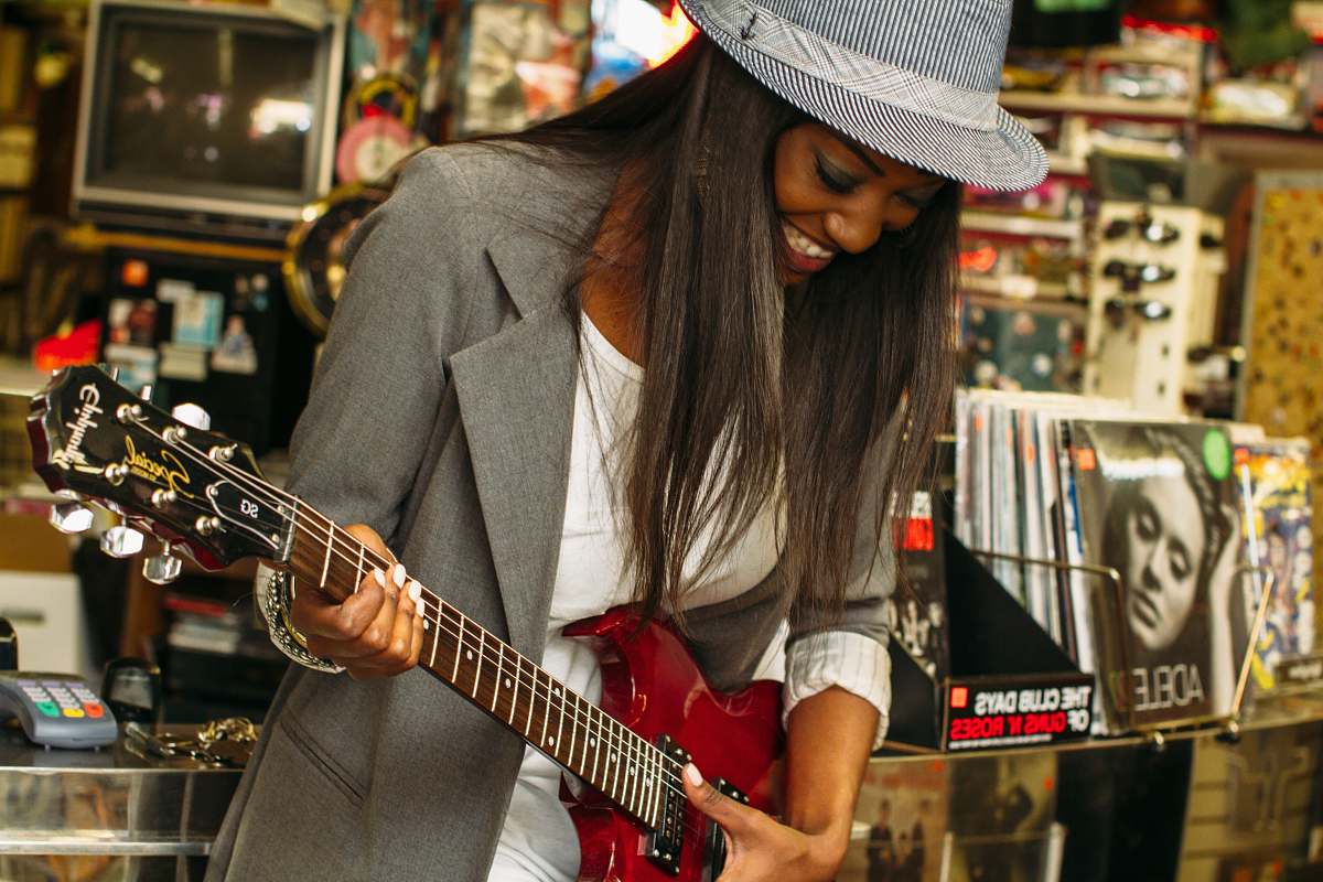 woman woman wearing grey suit jacket playing brown telecaster guitar near assorted poster lot music