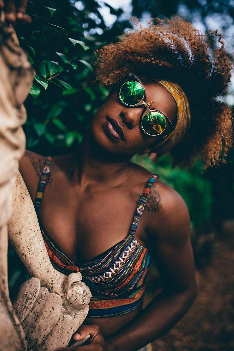 person woman wearing round sunglasses holding statue near tree close-up photography human