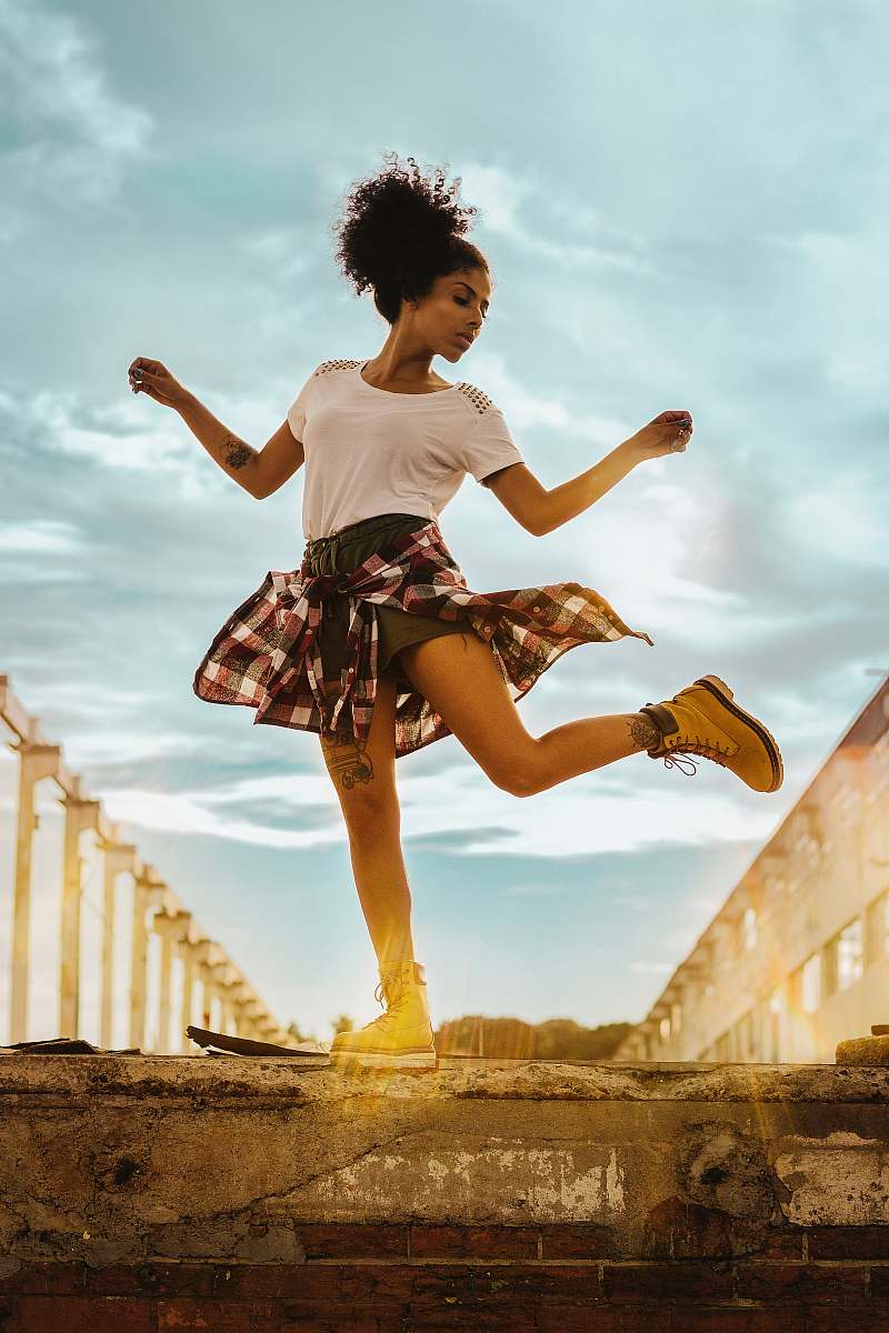 person woman wearing white crew-neck shirt and black shorts standing on one foot with hands lifted to the side dance