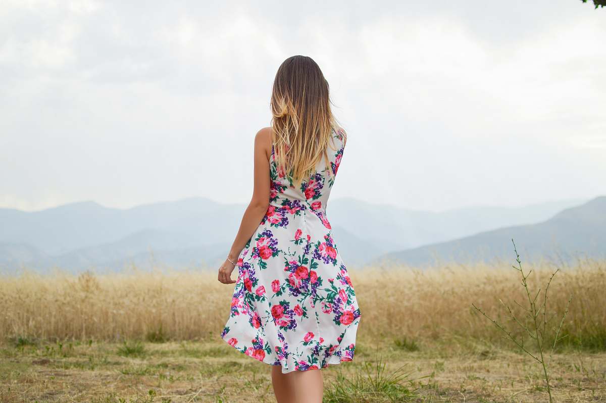 woman woman wearing white, purple, and pink floral dress standing near brown leaf grass field during daytime girl