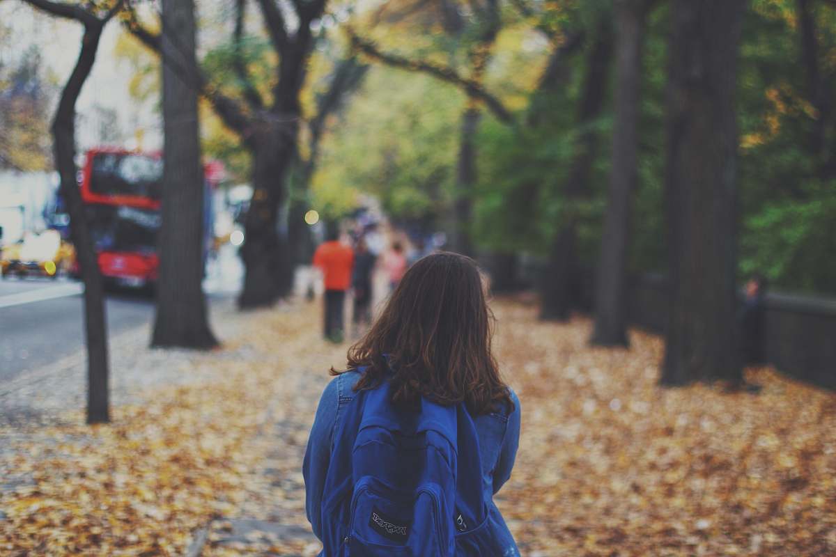 person woman with blue backpack on street full of fallen leaves human