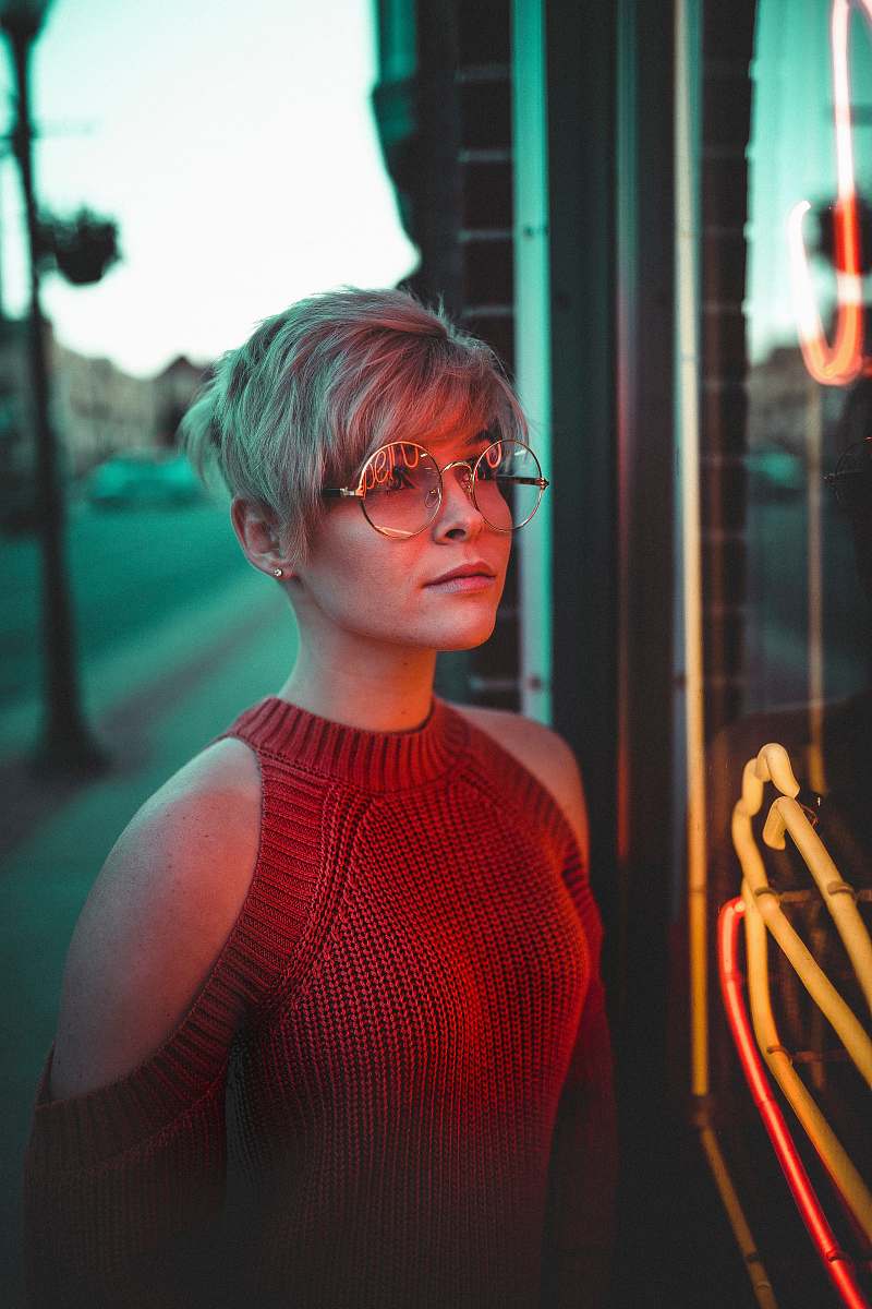 human woman with eyeglasses looking at glass panel with neon signage person