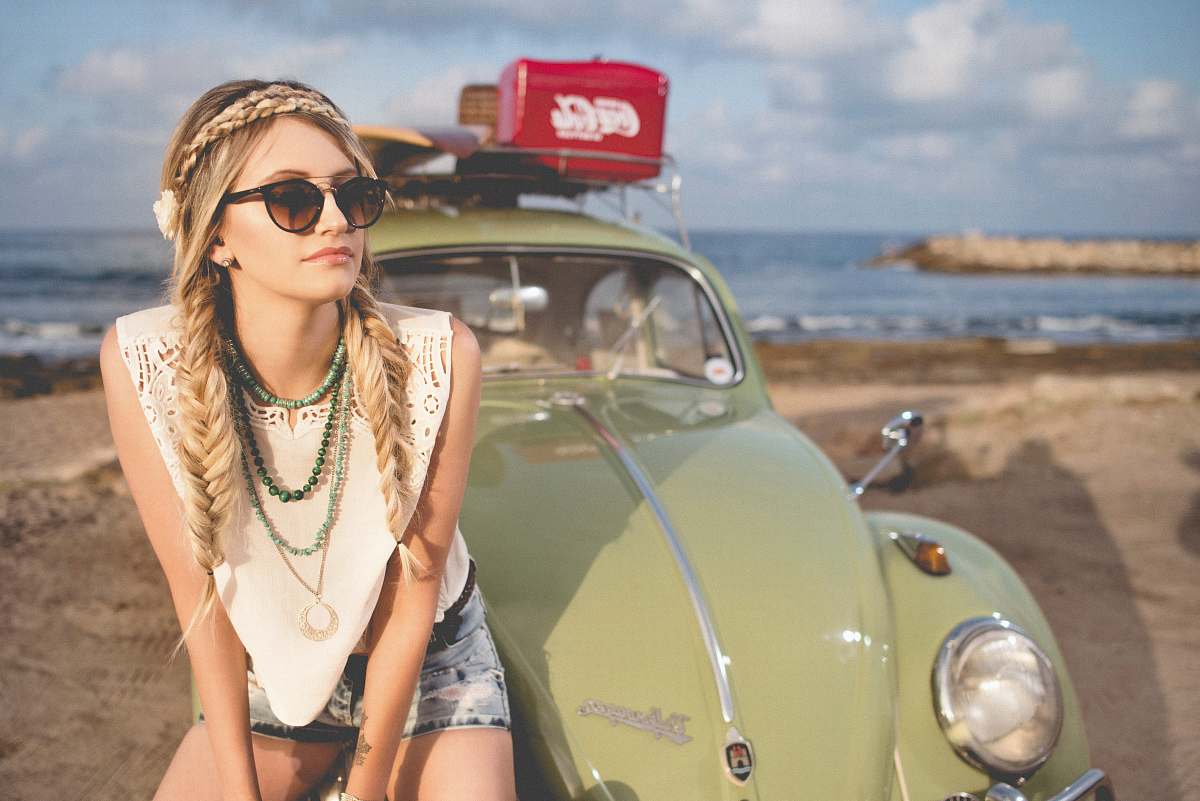 people selective focus photography of woman sitting on Volkswagen Beetle parked on beach shore girl