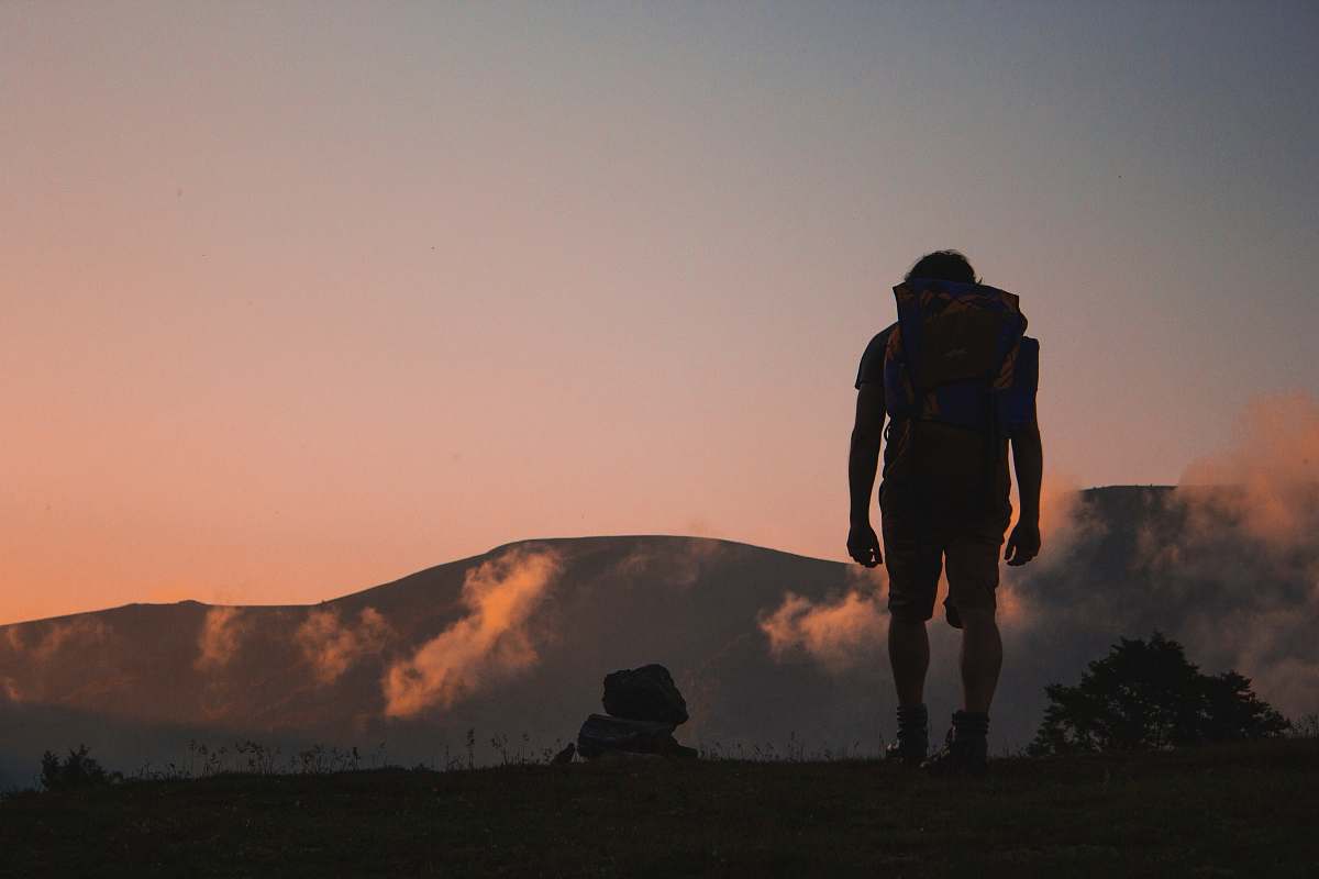 people silhouette of man walking along field leading to mountain human