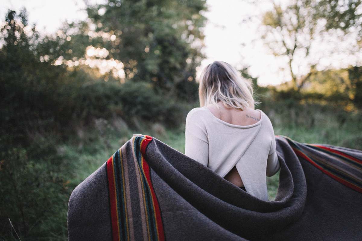 people standing woman holding gray blanket surrounded by green grass human