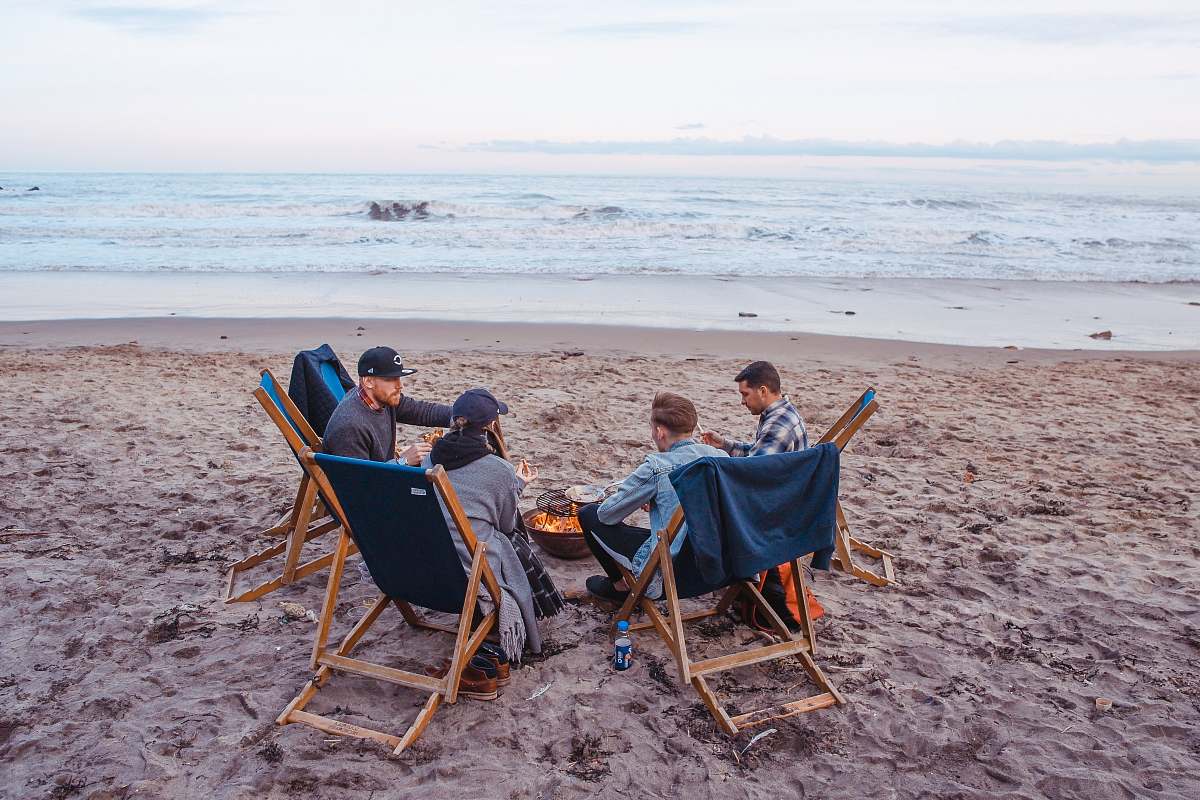 people three men and one woman sitting on beach lounge in front fire pit near seashore human