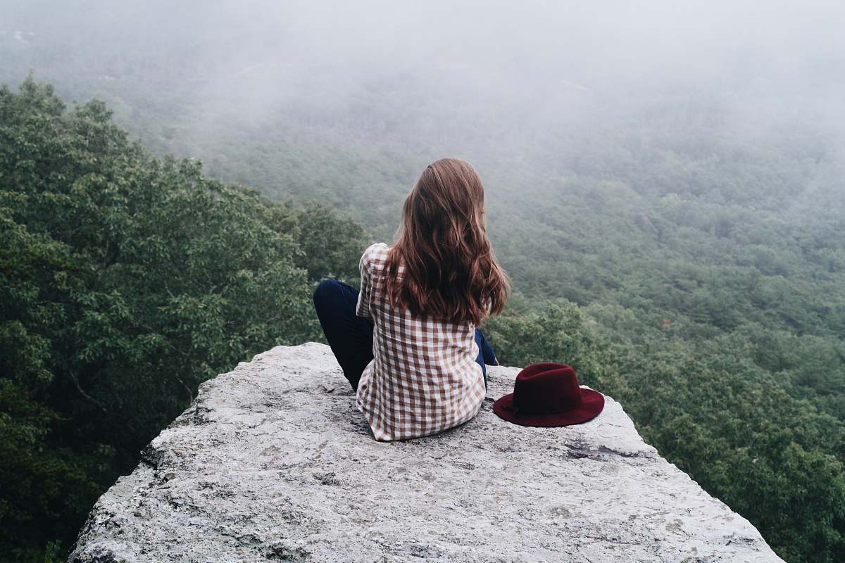 people woman sitting on top of gray rock woman