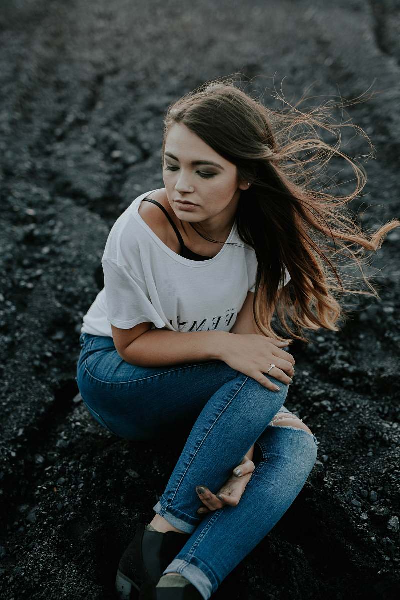 people woman wearing scoop-neck shirt and distressed jeans sitting on ground while holding knee human