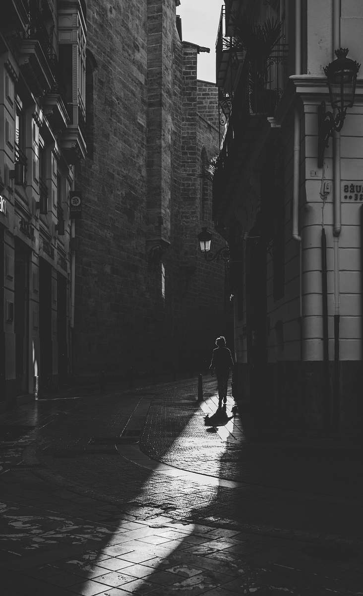 city grayscale photo of person standing in between buildings black-and-white