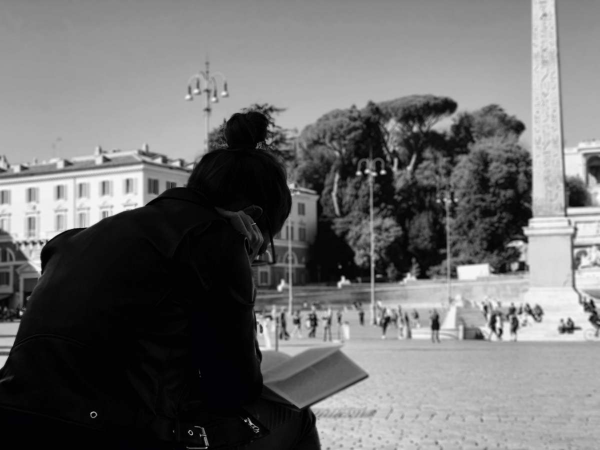 city grayscale photo of woman reading books black-and-white
