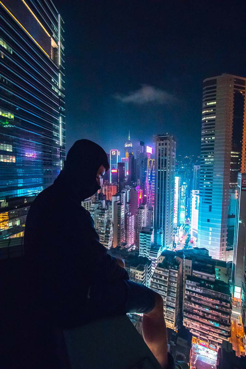 city man sitting on rooftop looking on city with high-rise buildings town