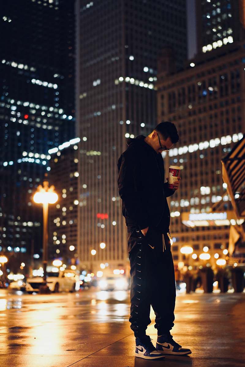 city man standing and holding disposable cup near building during nighttime metropolis