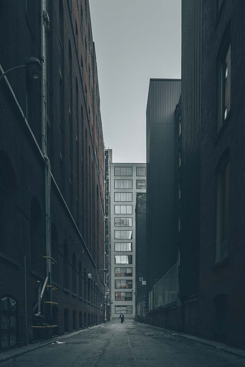 city man walking in the middle of city buildings under gray clouds grey