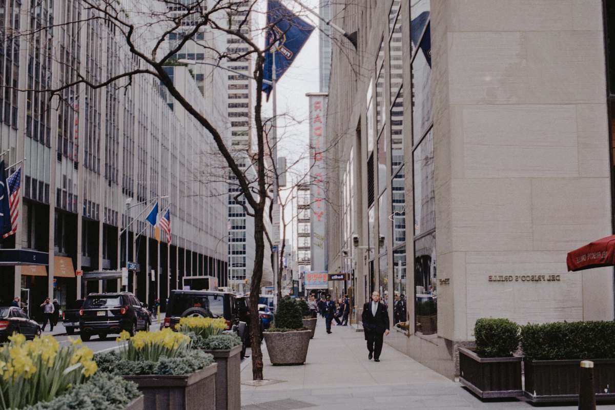 city man wearing suit jacket walking beside buildings road