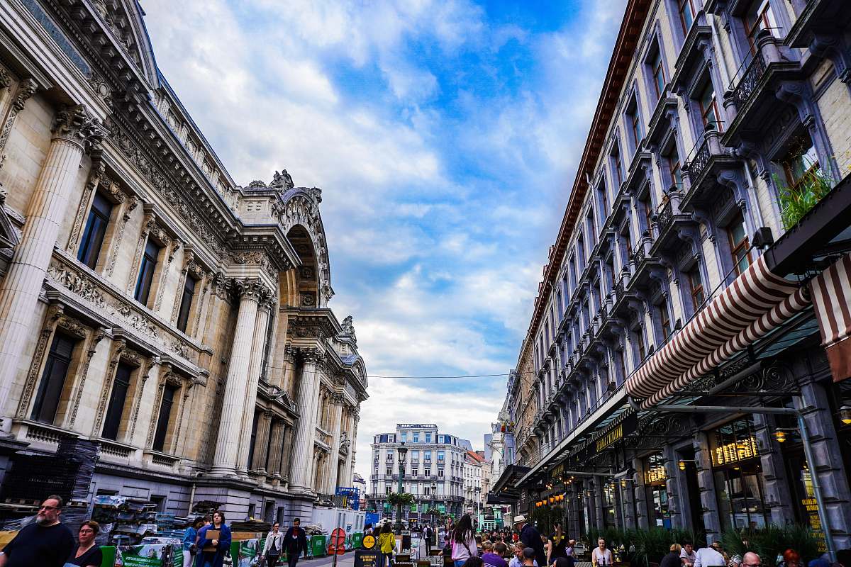 city people walking near brown historic buildings under white and blue sky during daytime downtown