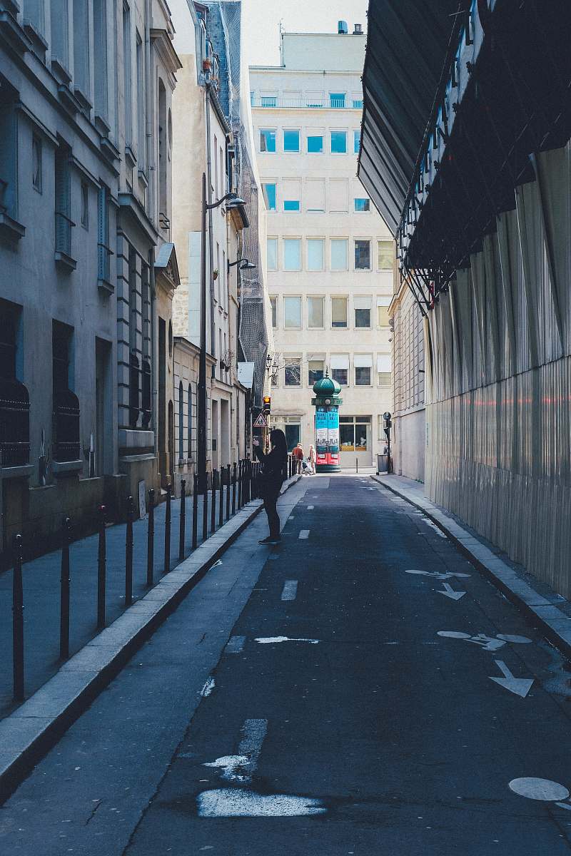 city person standing at the side of the road between buildings road
