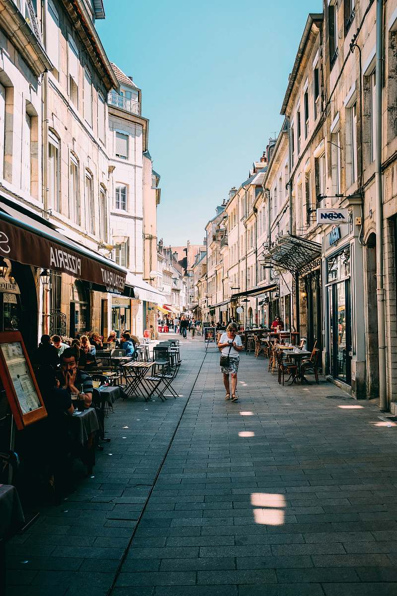 human person walking on alleyway with restaurant tables during daytime person