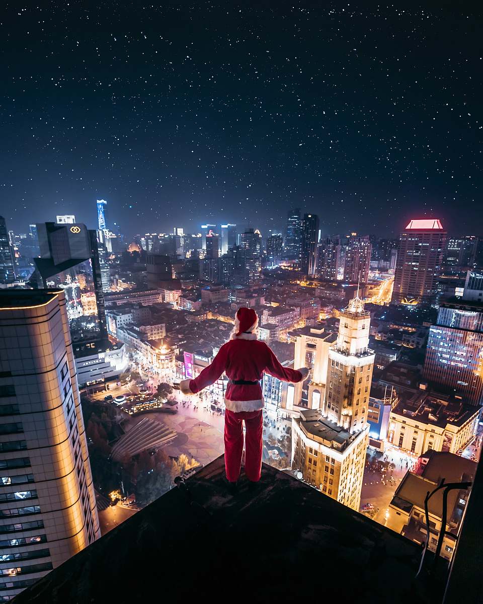 urban person wearing Santa Claus outfit standing on the edge of building at night time town