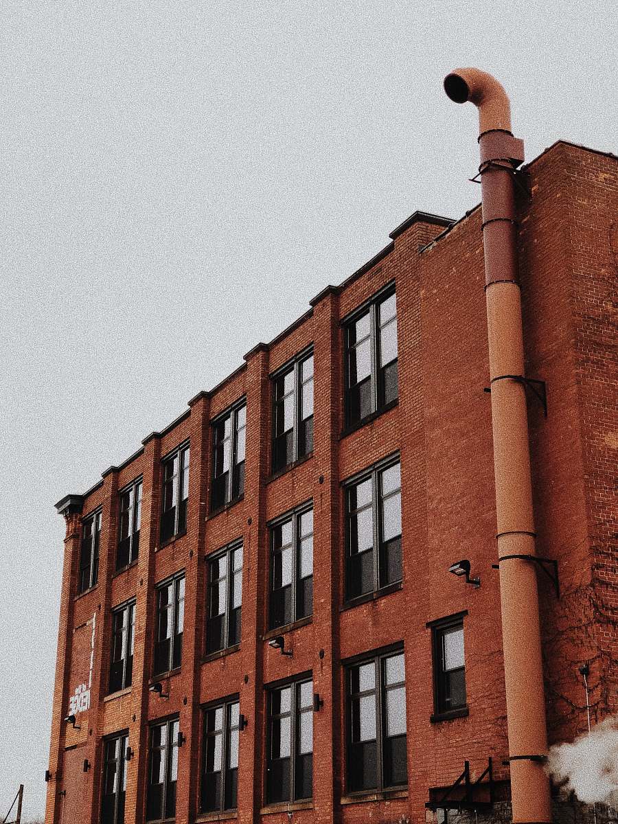 city red concrete building with grey exhaust pipe during daytime high rise