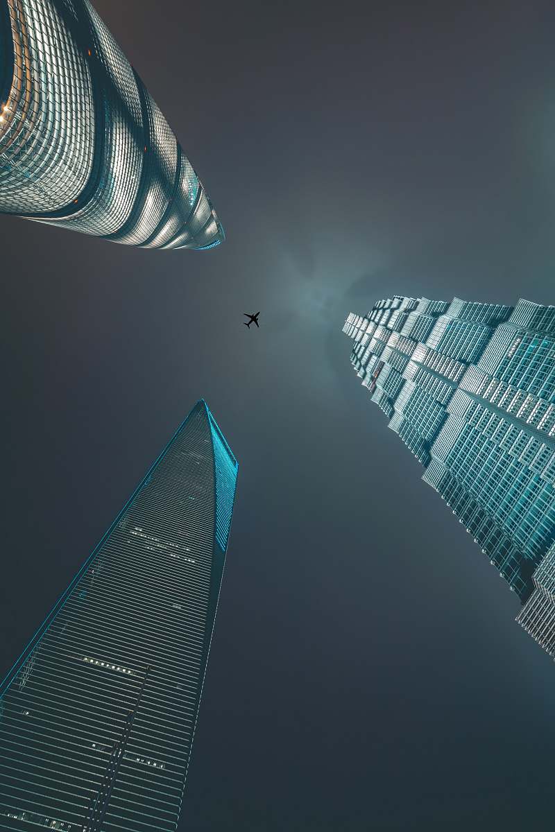 building airliner flying over three high-rise buildings town