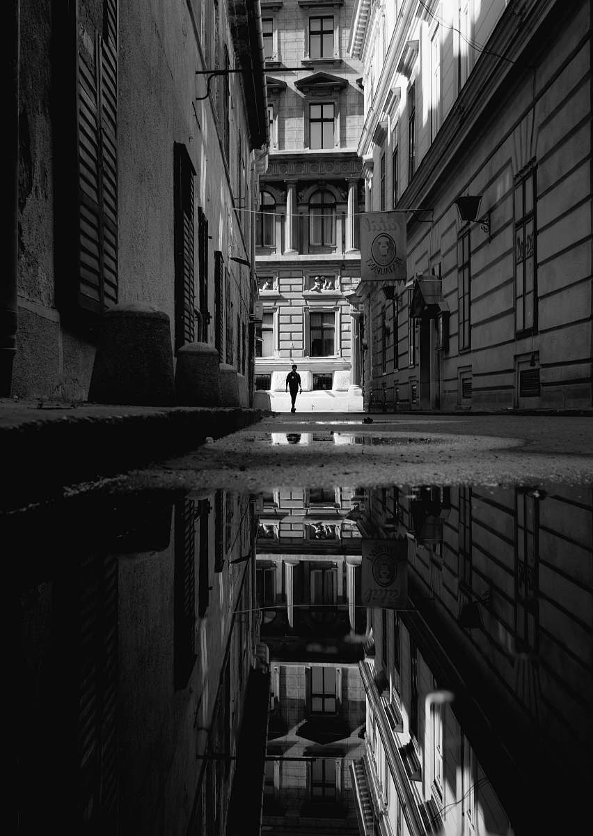 building grayscale photo of man about to enter the pathway in between of buildings black-and-white