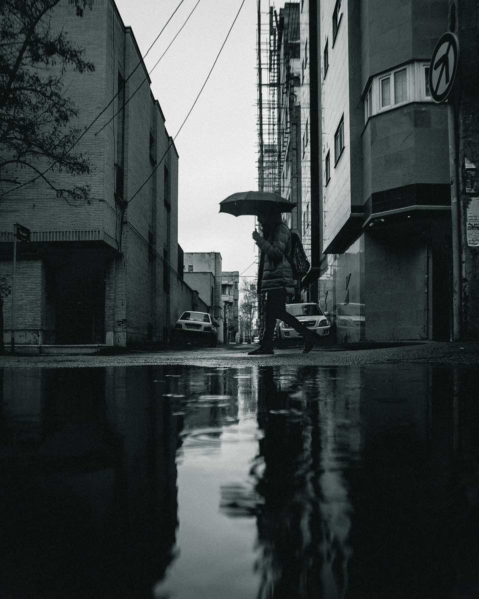 building greyscale photo of person walking and holding umbrella town