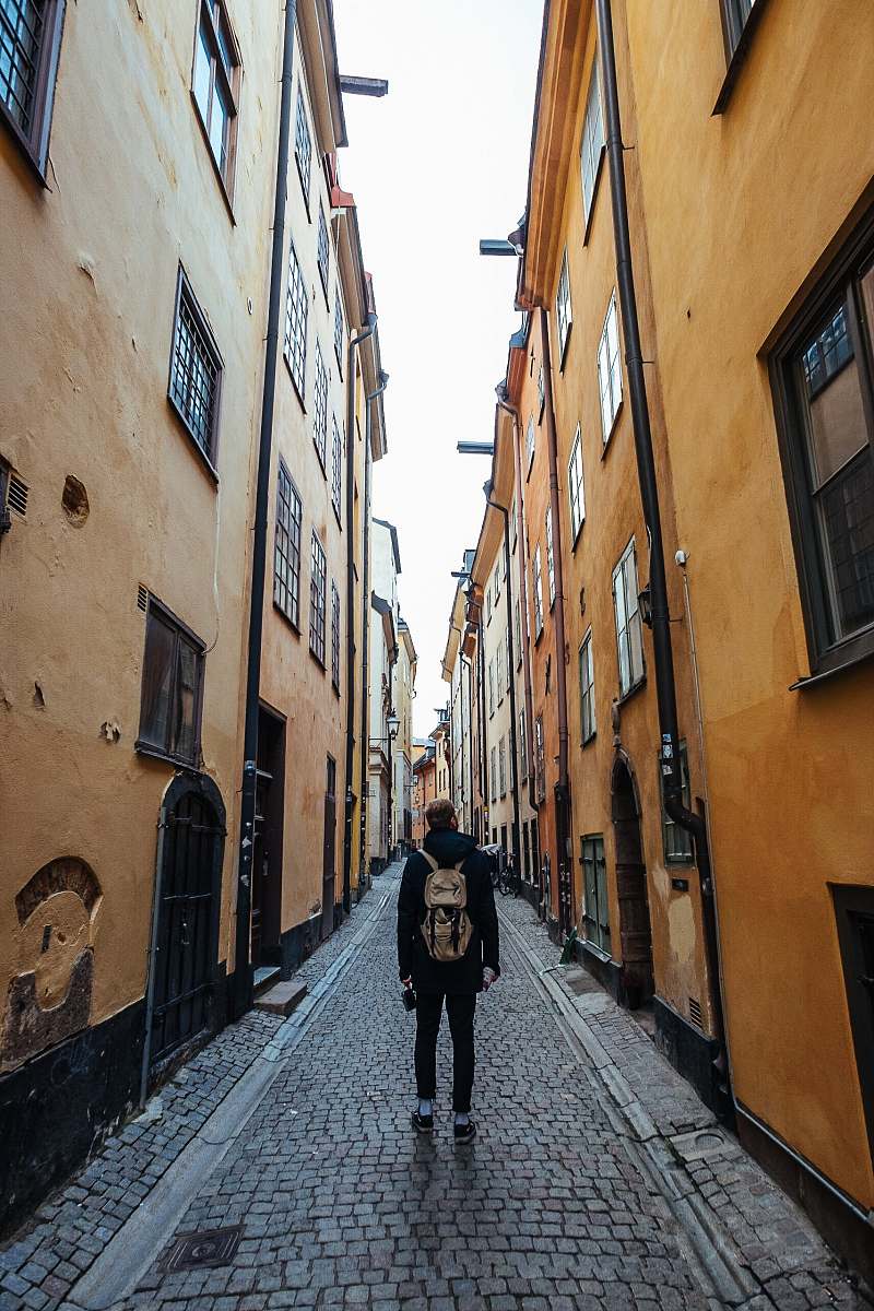 street man in black long-sleeved top and brown backpack walking on street alley