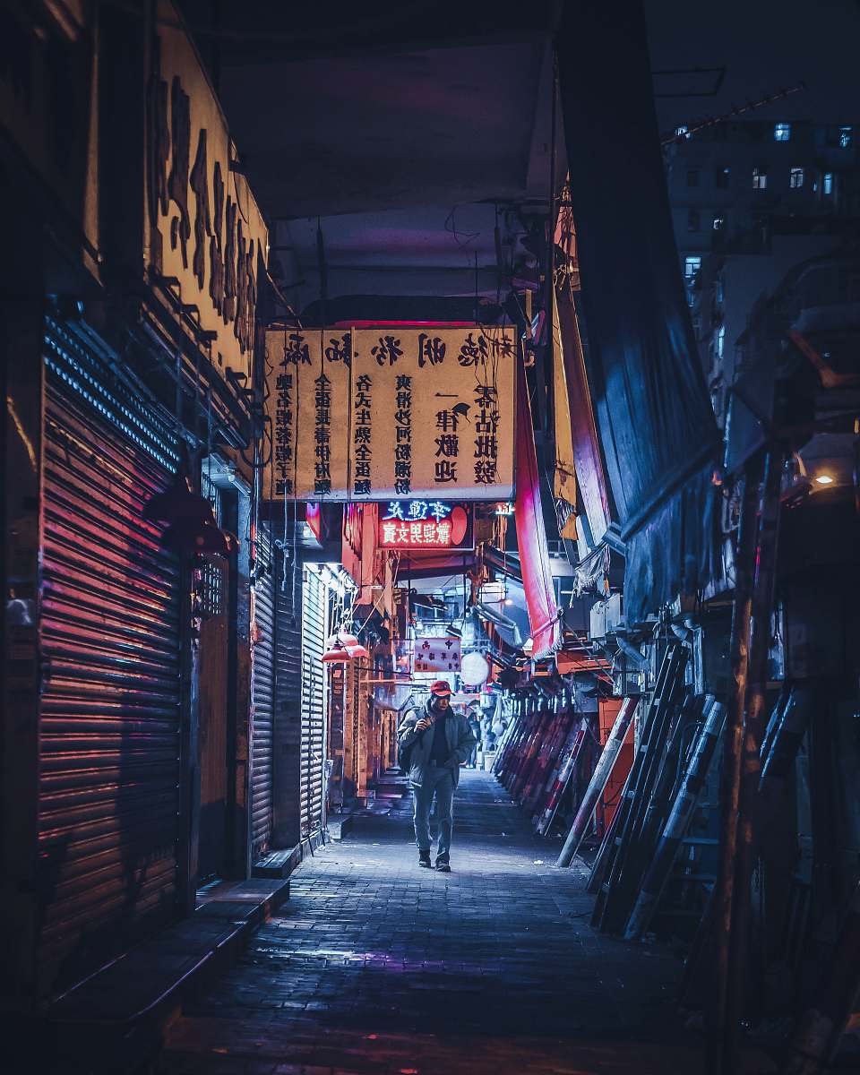urban man in denim jacket and jeans walking on pathway near buildings at night street