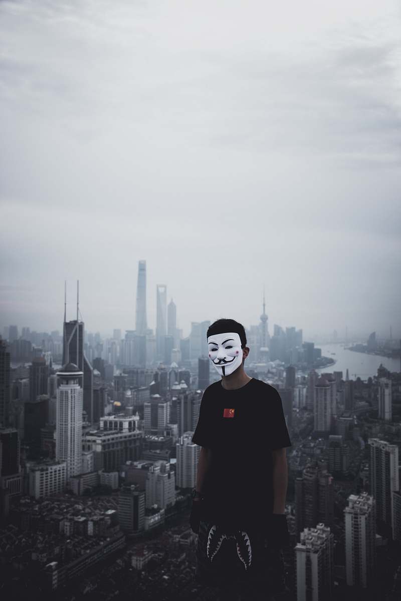 town man standing on top of building while wearing Guy Fawkes mask urban