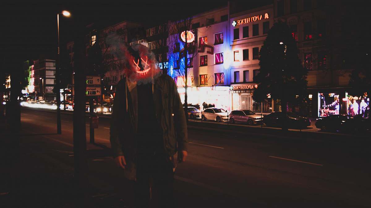 person man wearing red and yellow mask beside road during nighttime automobile
