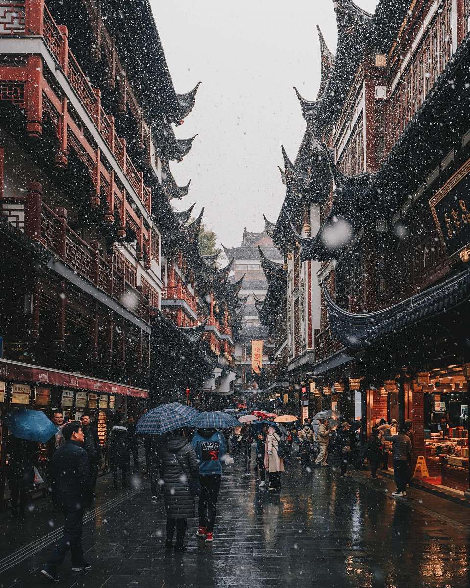 Immerse yourself in this dynamic urban street scene where pedestrians navigate the rain-soaked pavement, flanked by striking black and brown concrete structures. The image captures the essence of city life, showcasing the resilience and movement of individuals in an urban landscape. Perfect for use in articles about city living, urban planning, weather effects on daily life, and lifestyle photography.