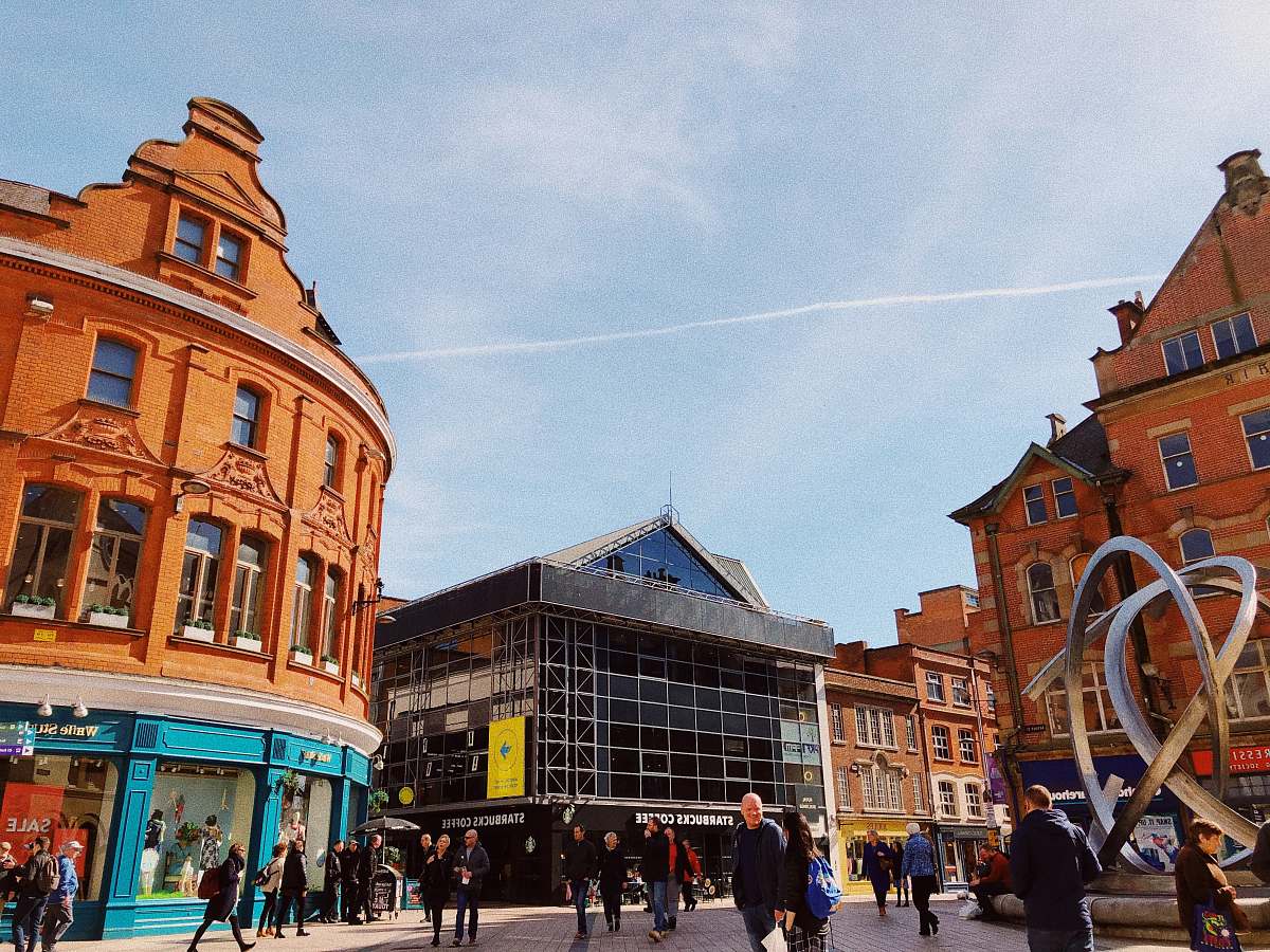 human people walking beside buildings under cloudy sky with contrail person