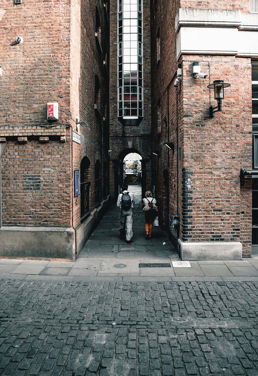 walkway two person walking in between concrete building during daytime path