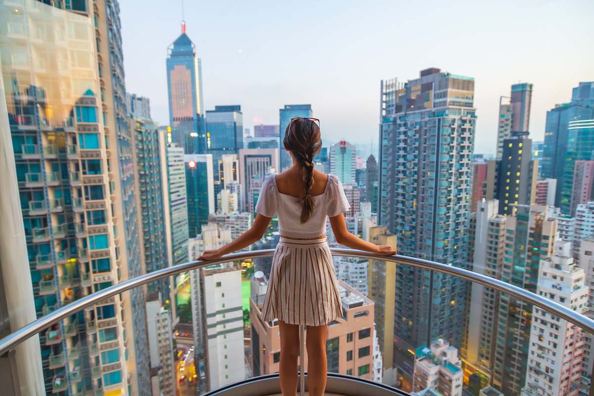city woman standing near gray stainless steel railings viewing city with high-rise buildings during daytime building