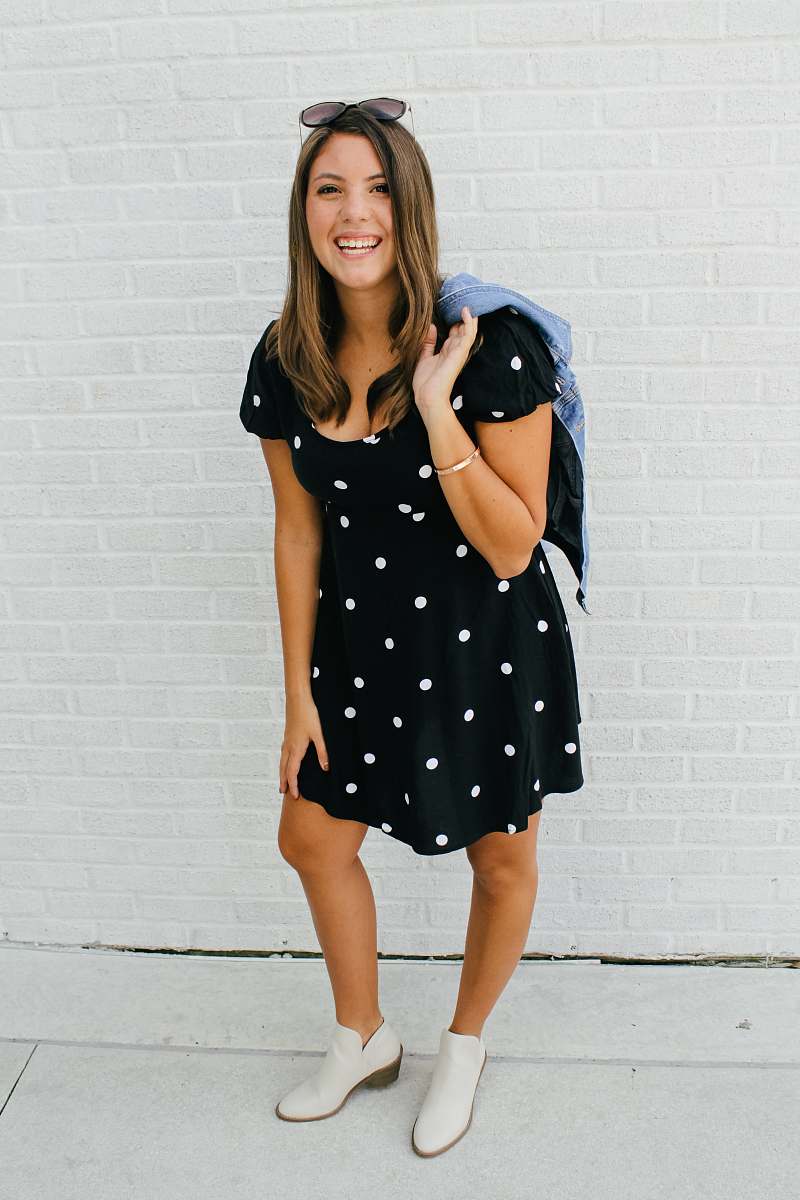 person woman in black and white polka dot dress standing beside white wall apparel
