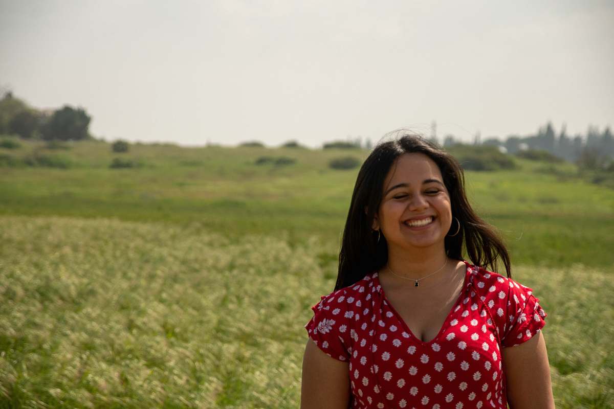 person woman in red and white polka dot shirt standing on green grass field during daytime smile