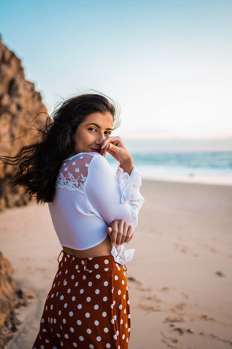human girl in white long sleeve shirt and black and white polka dot skirt standing on beach person