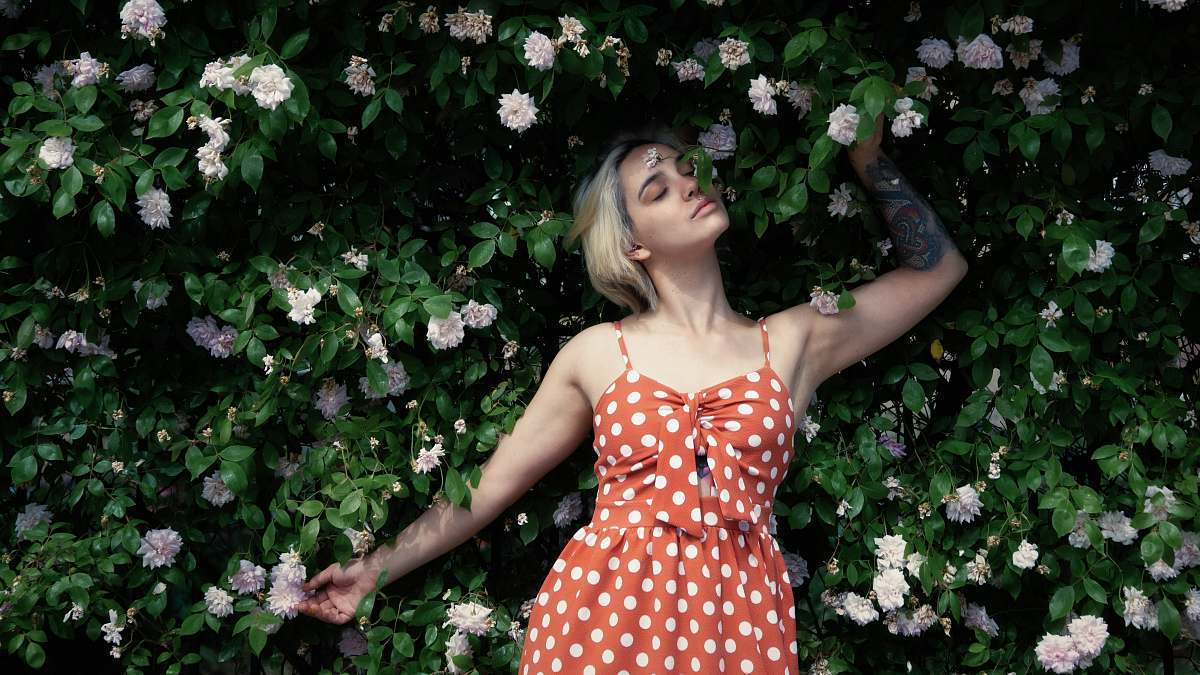 human woman in red and white polka dot dress standing beside white flowers person