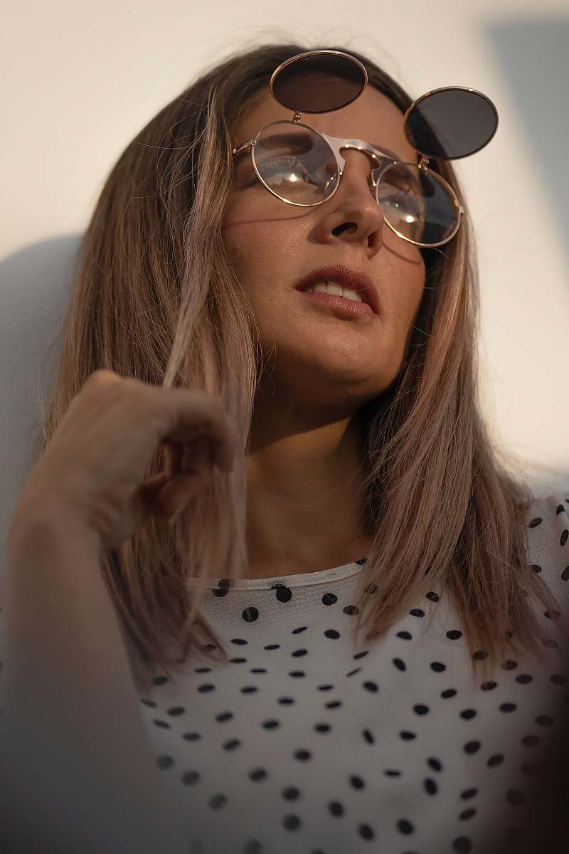 human woman in white and black polka dot shirt wearing silver framed aviator sunglasses person