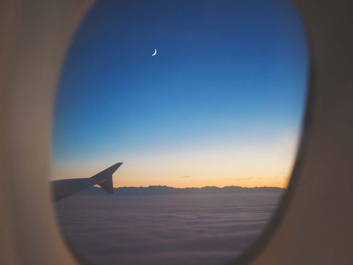 blue airplane window view of wing, clouds, and half moon window