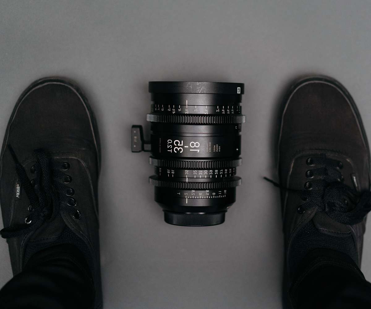 clothing black 18 35 camera zoom lens on floor near person wearing black Vans Authentic sneakers footwear