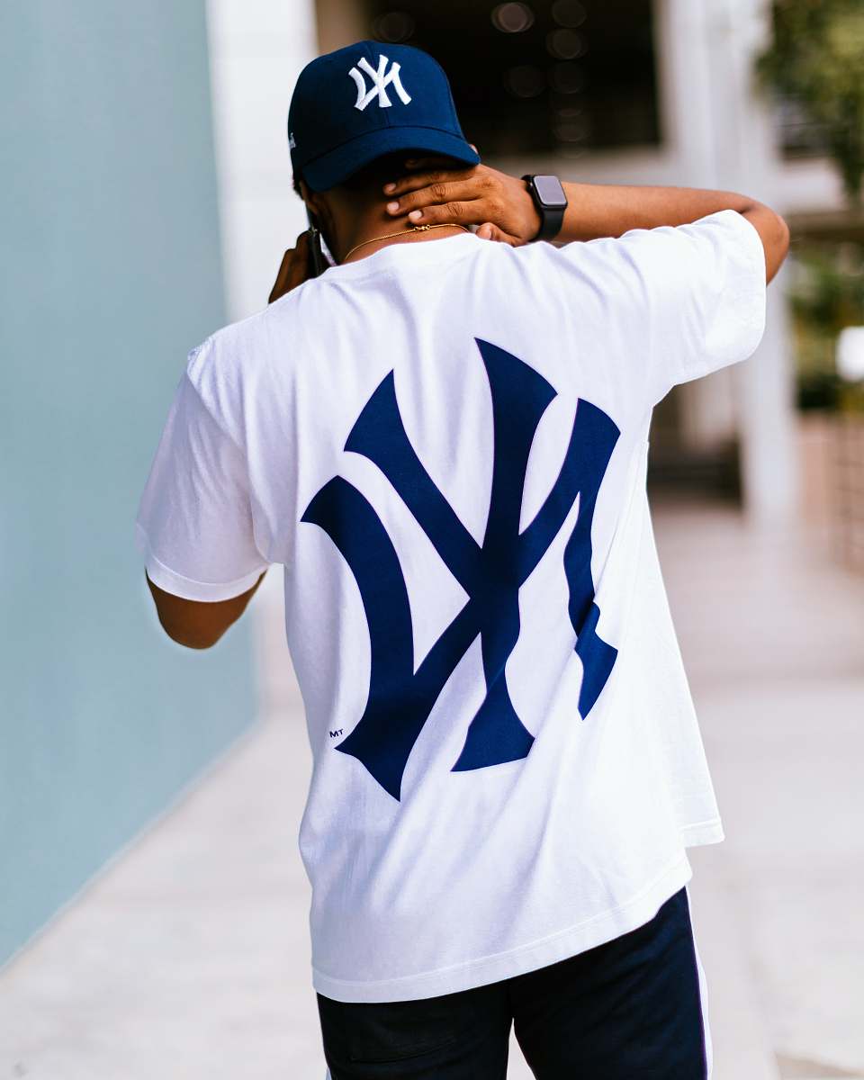 clothing man wearing white and blue New York Yankees t-shirt walking while touching his neck human