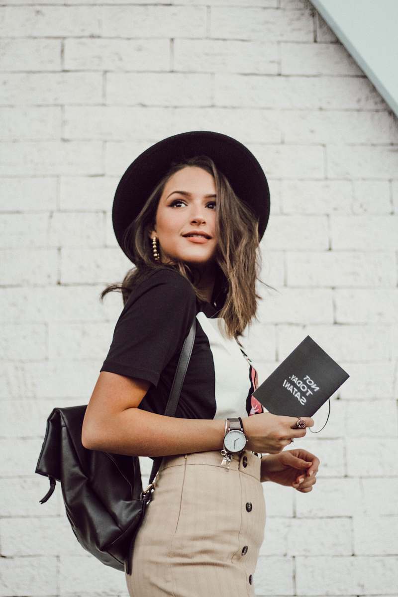 clothing woman in black blazer and brown dress holding booklet while looking into left side and smiling hat