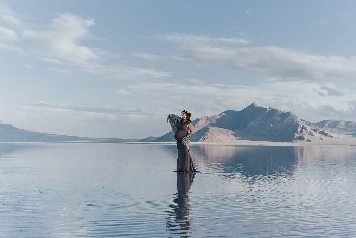 clothing woman standing on body of water with mountains at the distance outdoors