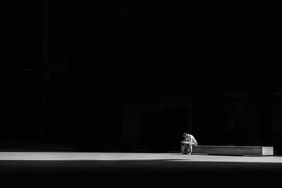 black grayscale photogaphy of man sitting on concrete bench dark