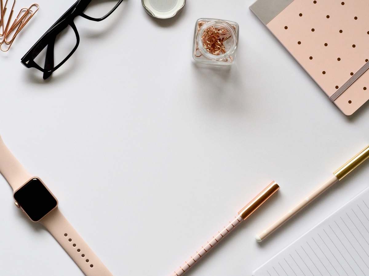 office flat lay photo of gold Apple Watch, clear eyeglasses and pens desk